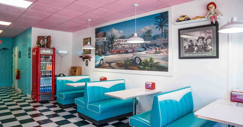Interior of a retro diner with turquoise booths, checkered flooring, and a pink ceiling