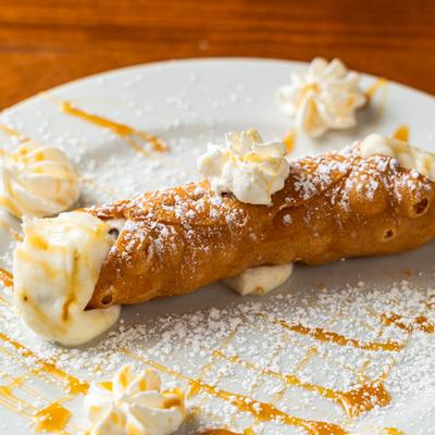 Cannoli with whipped cream, powdered sugar, and caramel drizzle.