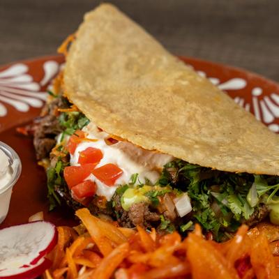 Beef taco with cilantro, sour cream, and diced tomatoes.