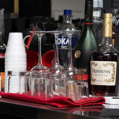 Bar counter with liquor bottles,  glasses, and plastic cups.