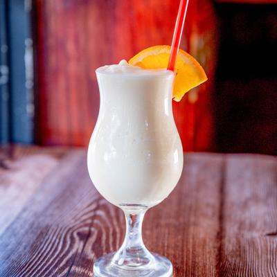 Pina Colada in glass with orange slice and red straw, set on a wooden table.