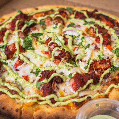 Loaded spicy meat pizza with melted cheese, vegetables, fresh herbs, and green sauce drizzle.