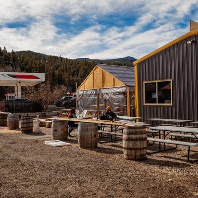 Outdoor seating area with tables and barrels surrounded by hills and trees.
