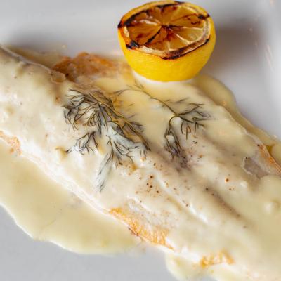 Baked haddock with fresh dill cream sauce, and grilled lemon half on a white plate.