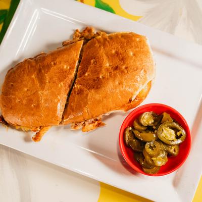 A Mexican torta sandwich cut in half with pickled jalapenos on the side.
