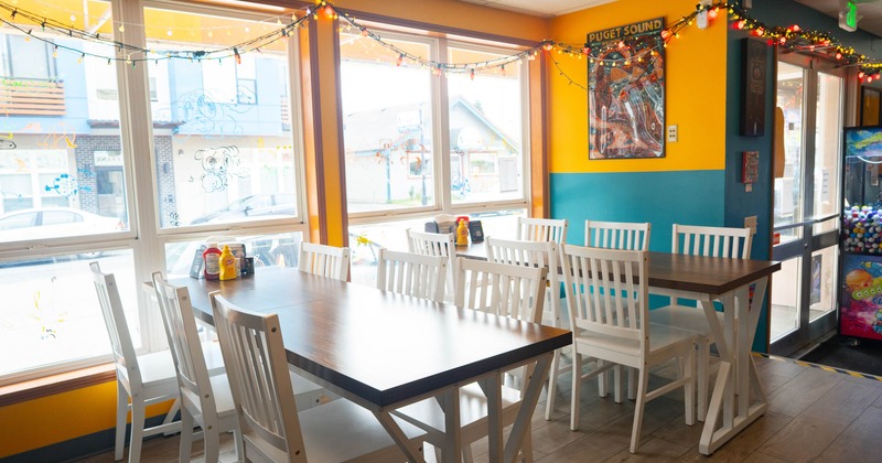 Interior with wooden tables and chairs, colorful walls and festive string lights along the windows.