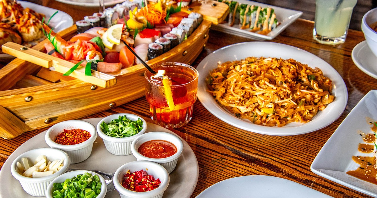 Table spread featuring a sushi boat, fried rice, various condiments and a cocktail
