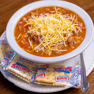 Bowl of chili, topped with grated cheese, with crackers on the side.