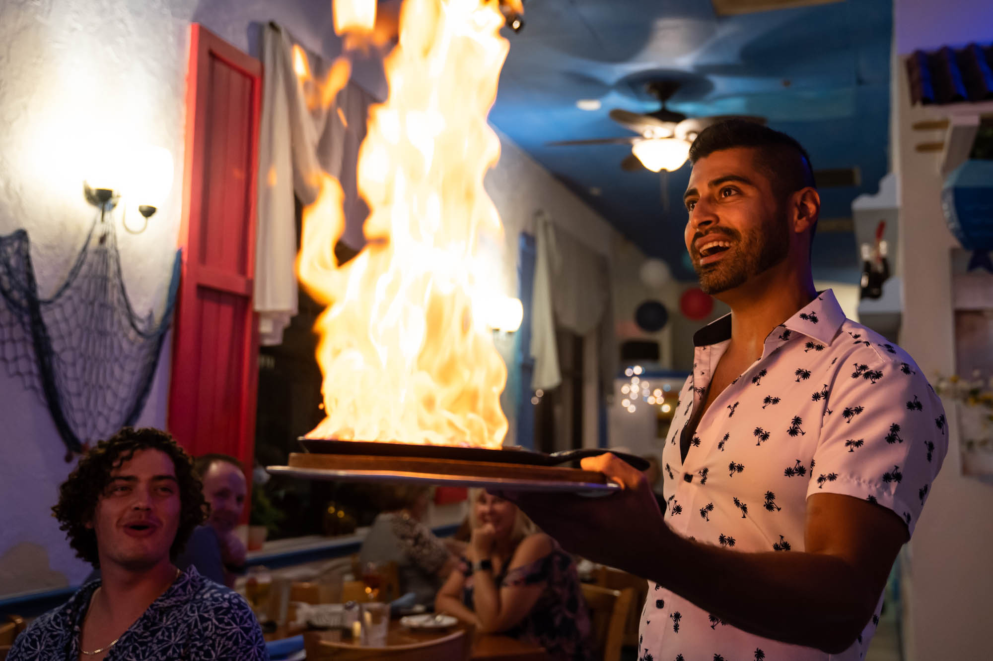 A server holding a plate with a flaming dish in front of amused guests