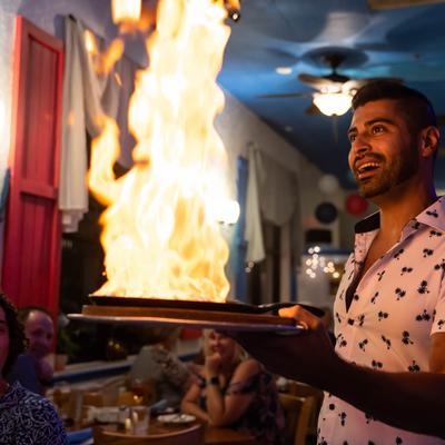A server holding a plate with a flaming dish in front of amused guests