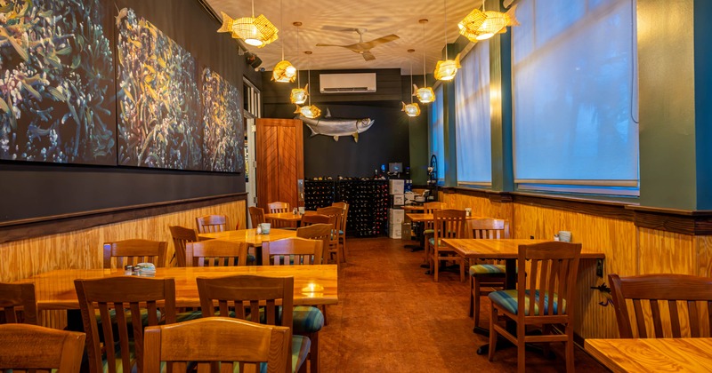 Interior of a restaurant featuring wooden tables and chairs, colorful marine themed artwork