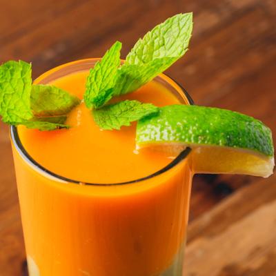 A glass of mango avocado smoothie, garnished with mint leaves and a lime slice.