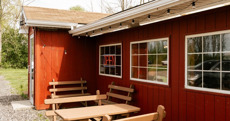 A red wooden building with a shingle roof, displaying an "OPEN" neon sign; picnic tables outside