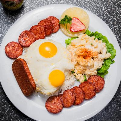 Hawaiian breakfast platter with eggs, rice, sausages, spam, potato salad, and pineapple.