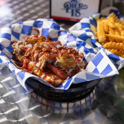 Pulled pork hot dog with pickles, ketchup, and  crinkle fries on the side.