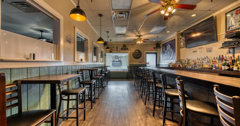 Interior of cozy seating area with high tables and stools along the wall and bar on the other side