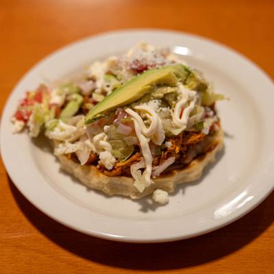 Open tostada topped with shredded meat, lettuce and avocado.