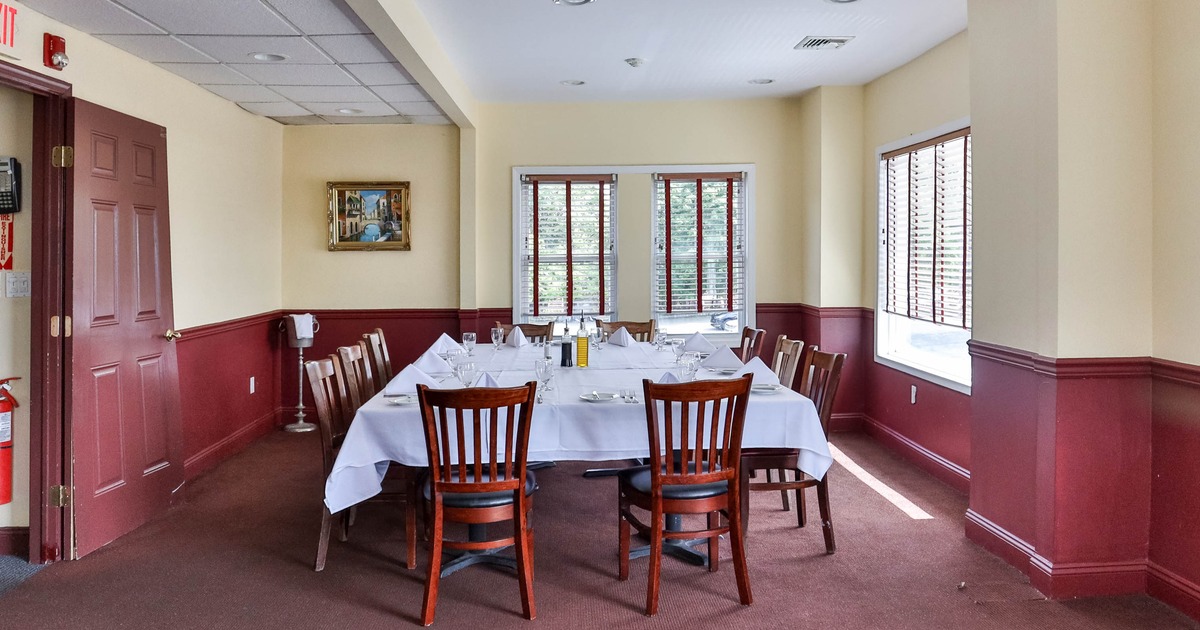 Dining room with a long table, surrounded by wooden chairs and large windows