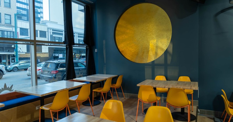 Interior of a modern café with yellow chairs, wooden tables, a large golden artwork
