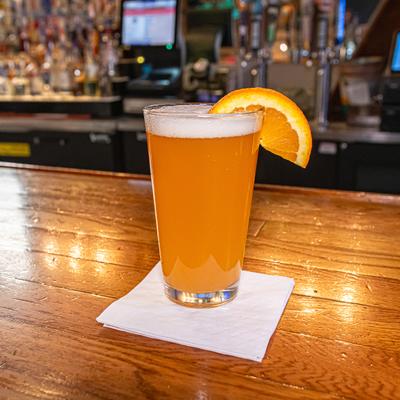 Glass of beer garnished with a slice of orange, served on the counter.
