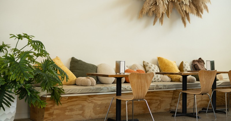 A long built-in bench with soft cushions, wooden tables, and minimalist chairs