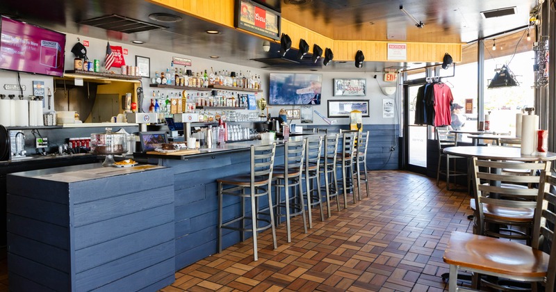 Interior, bar area, bar with stools, drink shelves, tile flooring, restaurant entrance