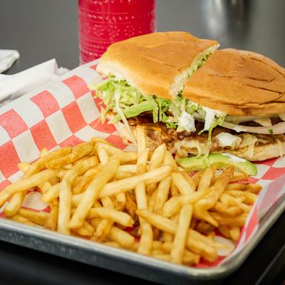 A large Mexican torta sandwich served with crispy french fries on paper.