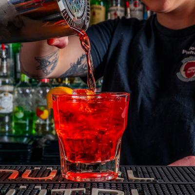 A bartender pouring red drink into a glass on bar counter.