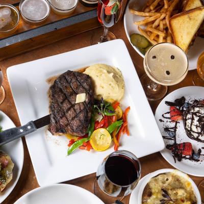 Ribeye steak with mashed potatoes surrounded by various drinks and dishes.
