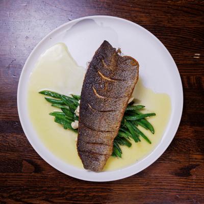 Seared trout served over green beans and lemon garlic sauce on a white plate