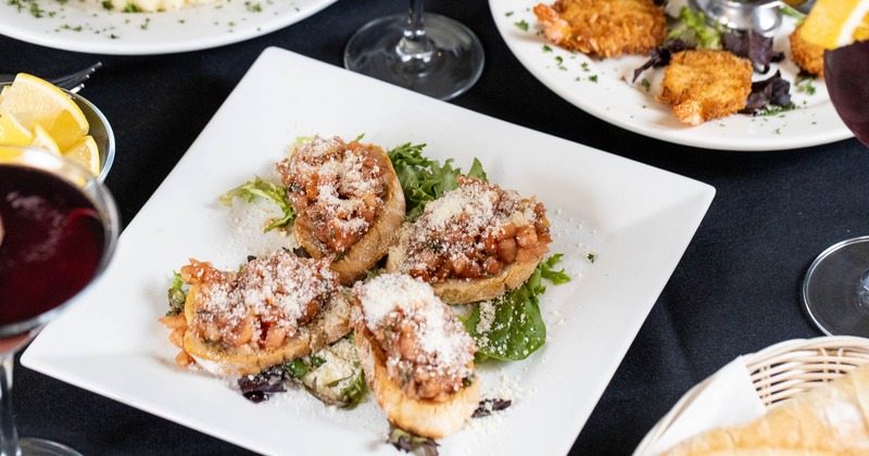 Bruschetta plate surrounded by assorted dishes