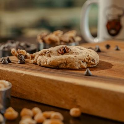 Butter pecan cookie on a wooden board surrounded by chocolate chips.