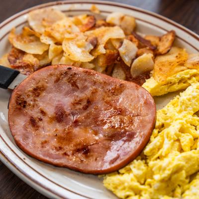 Breakfast platter with ham steak, scrambled eggs, and potatoes.