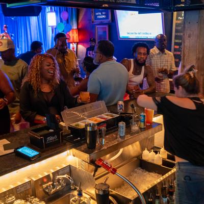 Patrons socializing at a bar with a view of the bartender and a cocktail station.