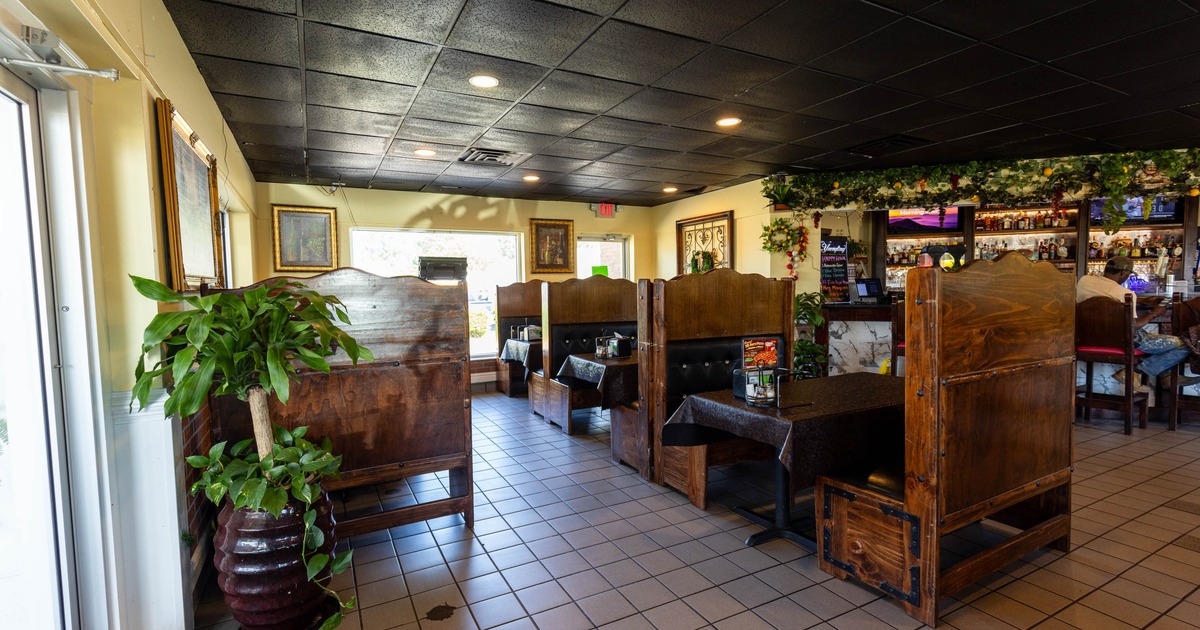 Interior of a restaurant with wooden booths, tiled floor and a bar area.
