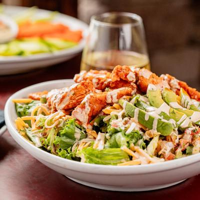 Buffalo chicken salad with mixed greens, avocado, and ranch drizzle.