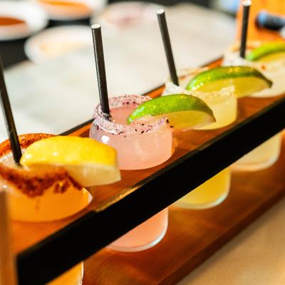 Margarita flight with multiple colorful cocktails served in small glasses on a wooden holder.