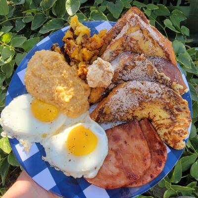 A breakfast plate featuring two fried eggs, French toast, grits, and ham.