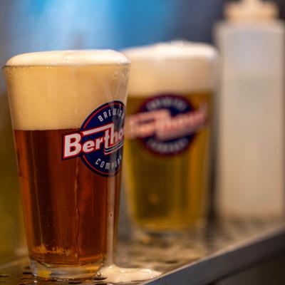 Pint of beer with overflowing foam in a branded glass.