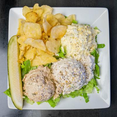 Scoop of tuna, chicken and egg salad with chips and pickle.