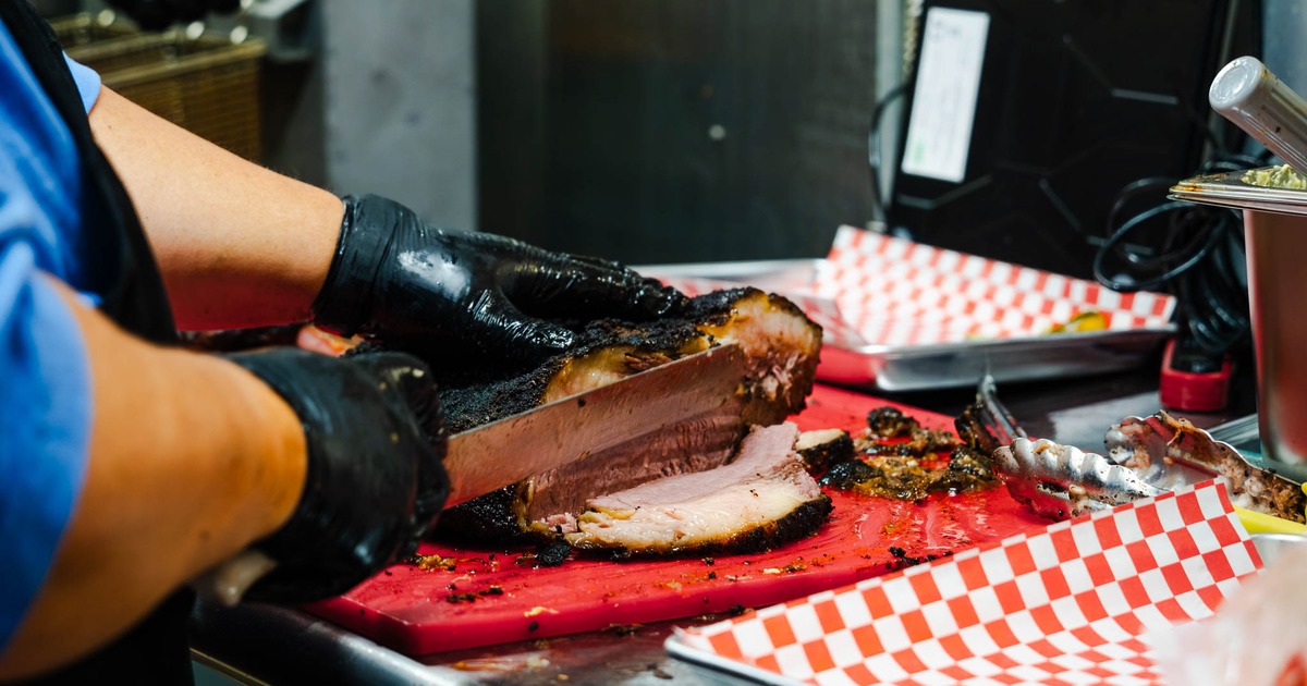 Pitmaster slicing a slow-smoked beef brisket, close-up
