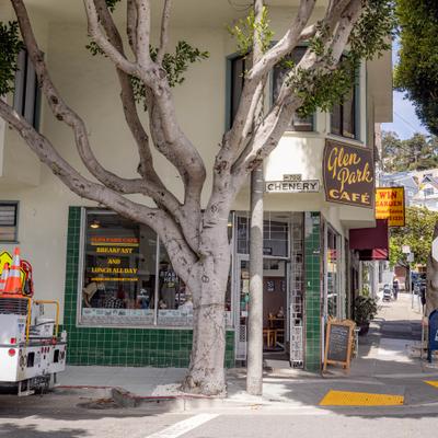 Cafe storefront shaded by a large sidewalk tree.