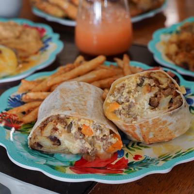 Breakfast burrito with fries on a colorful plate.