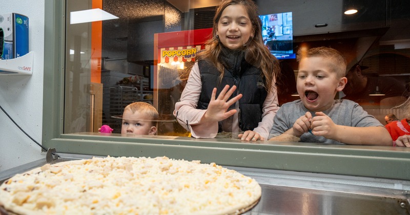 Delighted children from the street side of the glass watch the pizza being prepared inside