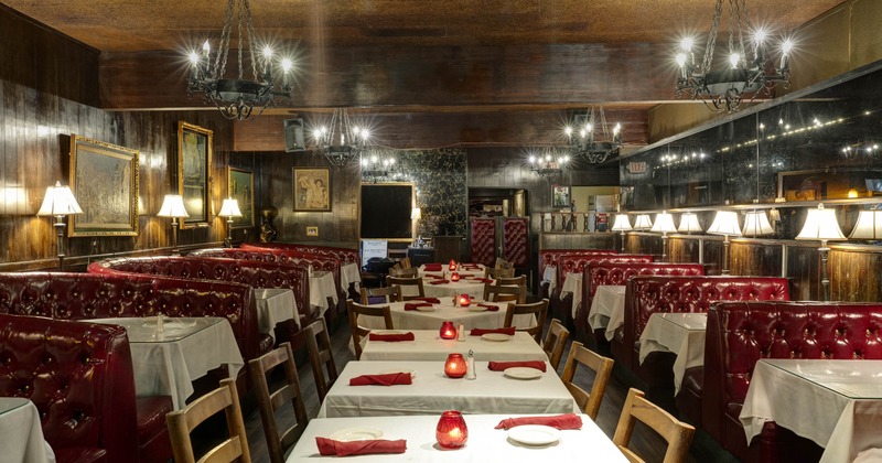 A vintage interior with red leather booths, wooden tables and chandeliers