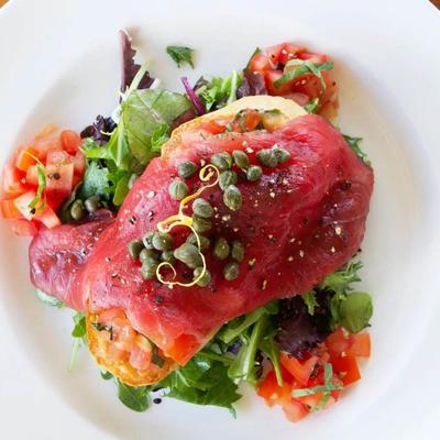 Ahi tuna, served over greens and toasted bread, garnished with capers and diced tomatoes.