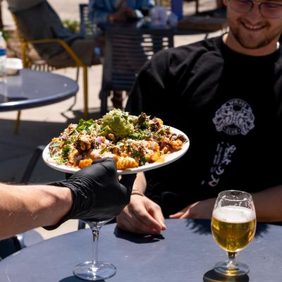 An employee serves a plate of Asada Fries to a group of customers at an outdoor table.