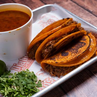 Beef birria tacos with consomme and chopped cilantro.