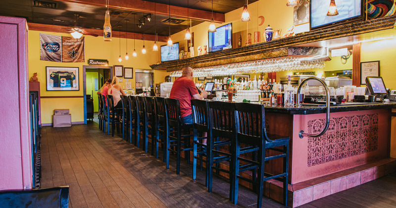 Bar area with wooden stools, liquor bottles, glassware, and seated customers