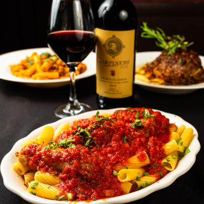 Pasta topped with a rich red tomato sauce, served alongside a glass of red wine.